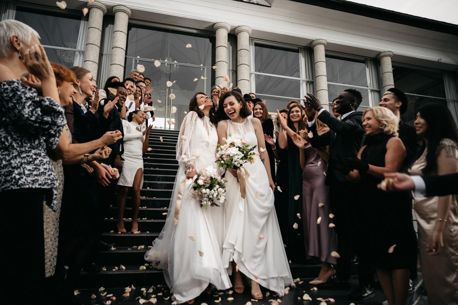 Two brides exit church excited after their San Diego LGBTQ+ beach wedding, guests smile and cheer for them with professional DJ entertainment