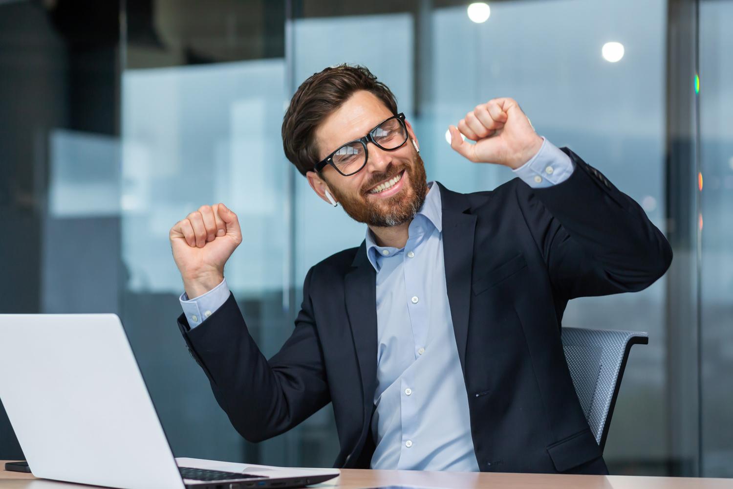 White man with arms raised in front of laptop